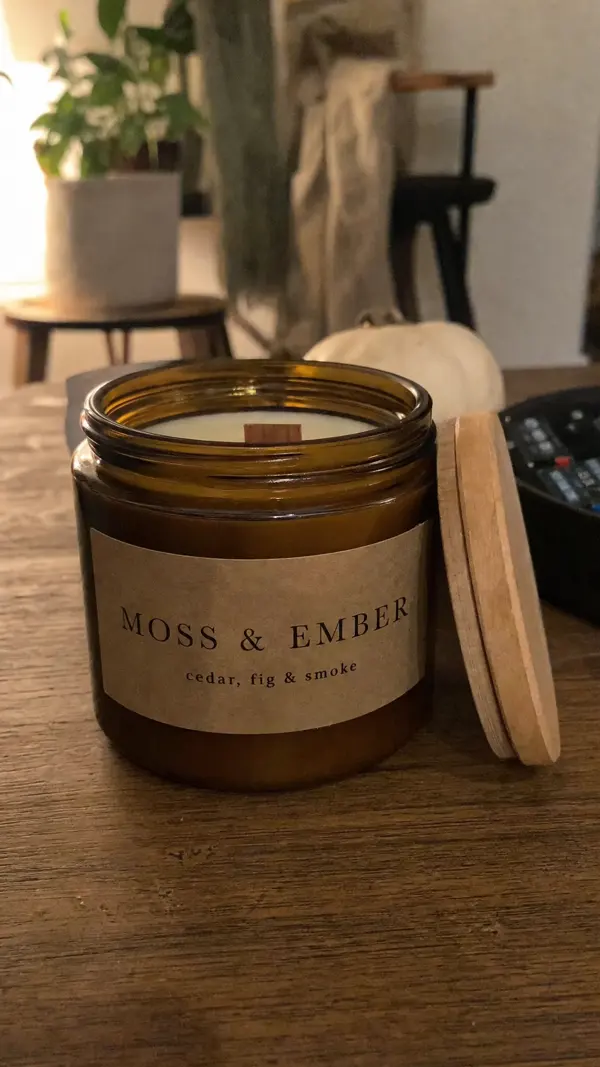 The Moss & Ember candle: an amber glass jar with a wooden lid and a kraft label reading cedar, fig & smoke